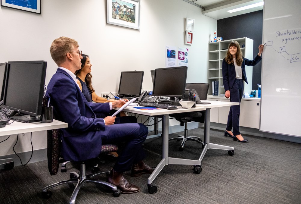 Herbert Smith Freehills Graduate - Two young professionals sitting while another professional explaining on the board.